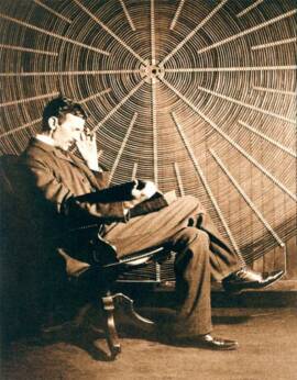 Nikola Tesla sitting in front of a large spiral coil